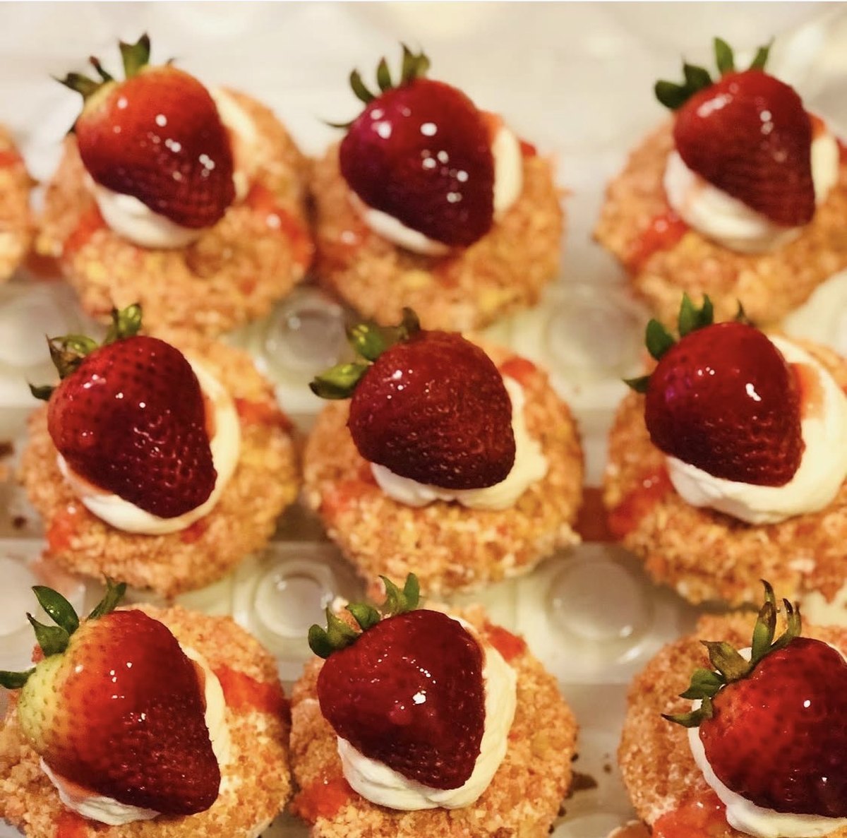 Individual strawberry shortcake bites with whipped cream, glazed strawberries and crumb coating on a white platter