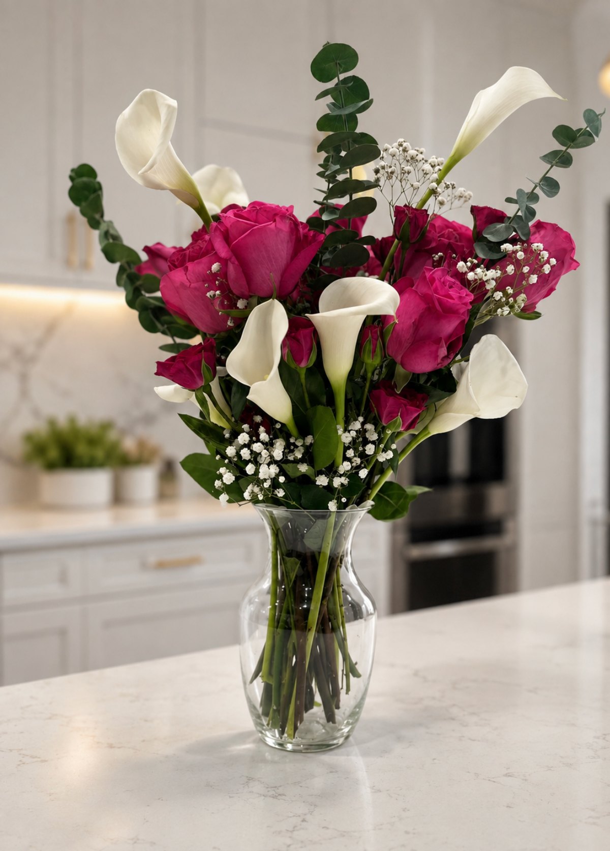 Event floral arrangement of magenta roses, white calla lilies and baby's breath in a glass vase on a marble counter