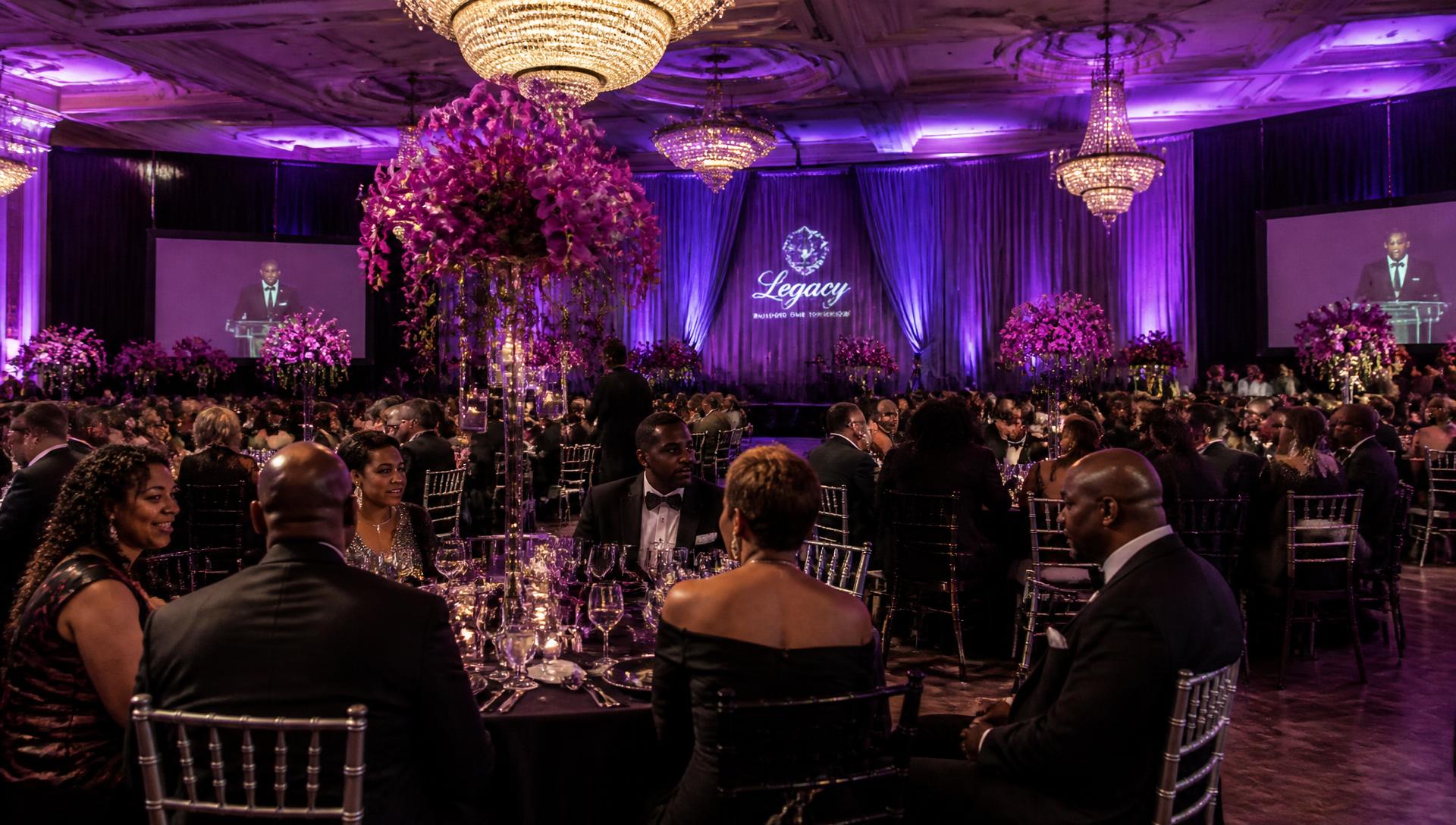 Elegant gala ballroom with tall purple orchid centerpieces and violet uplighting